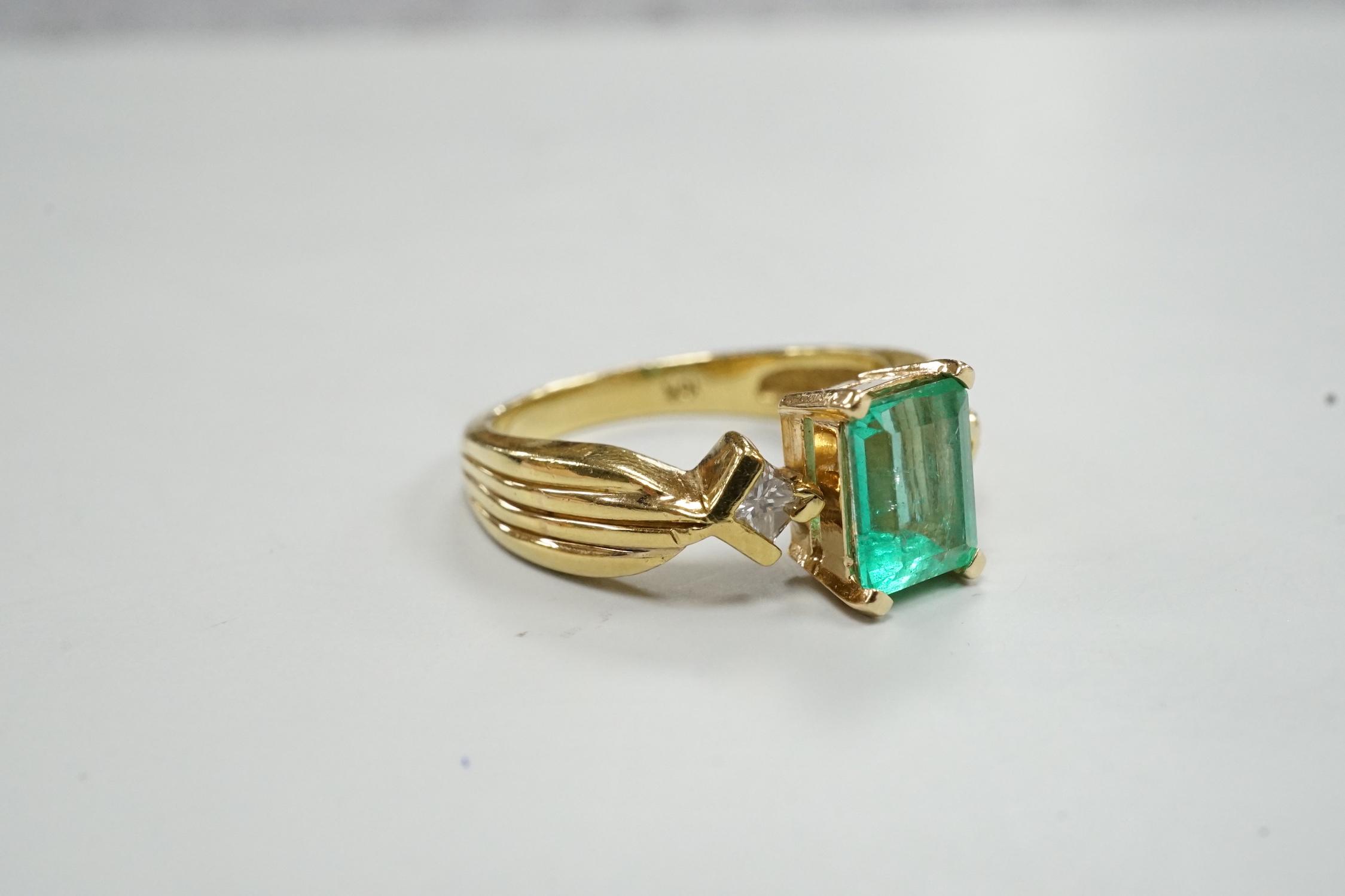 A modern 18k yellow metal and single stone emerald set ring, with two stone diamond set shoulders, size O, gross weight 5.8 grams.